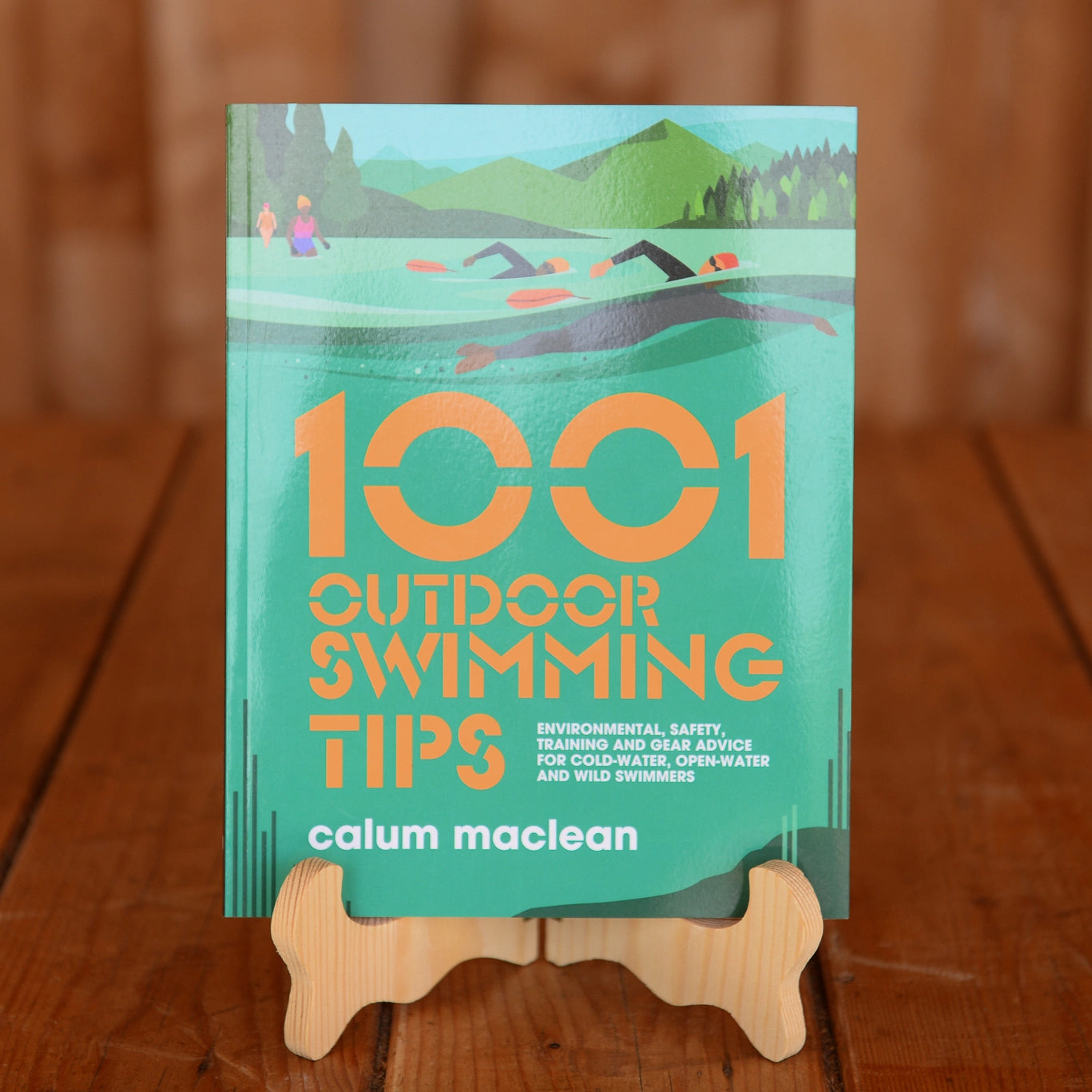 The book 1001 Outdoor Swimming Tips by Calum Maclean displayed on a book stand on a wooden table