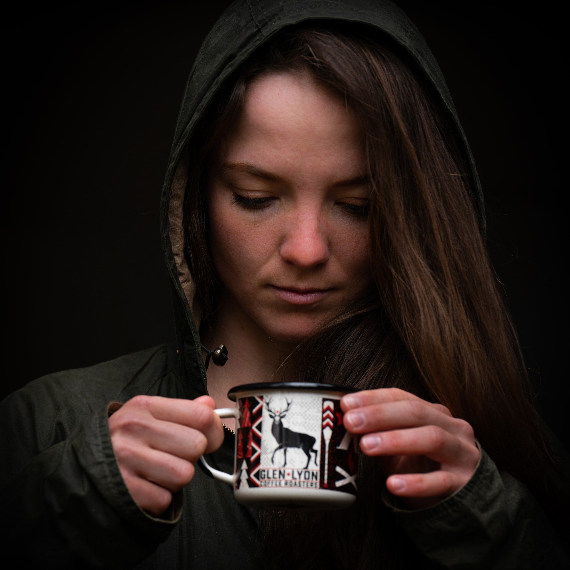 Closeup of a woman wearing a hooded jacket holding a Glen Lyon Coffee enamel camp mug