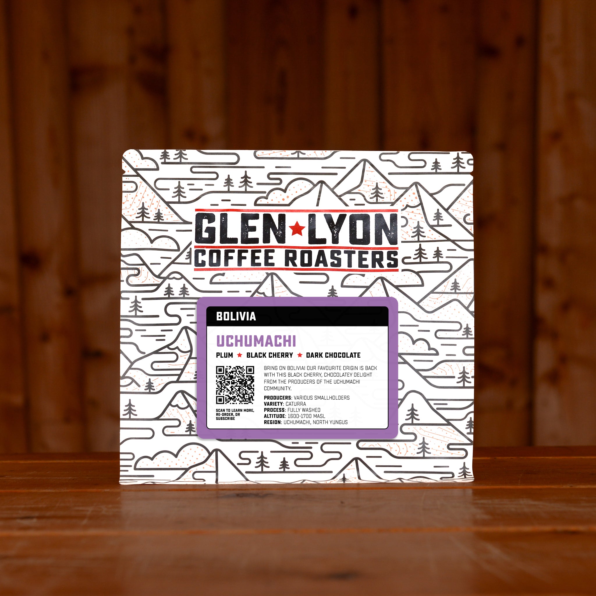 Purple Bolivia Uchumachi information sticker on a Glen Lyon branded coffee bag, sitting on a wooden table with a wood panel background.