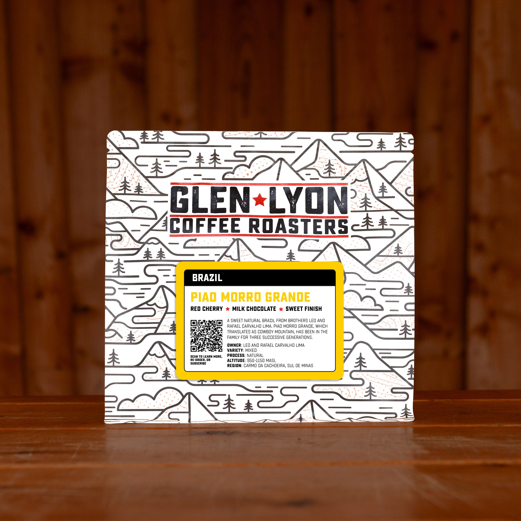 Bright yellow Brazil Piao Morro Grande information sticker on a Glen Lyon branded coffee bag, sitting on a wooden table with a wood panel background.