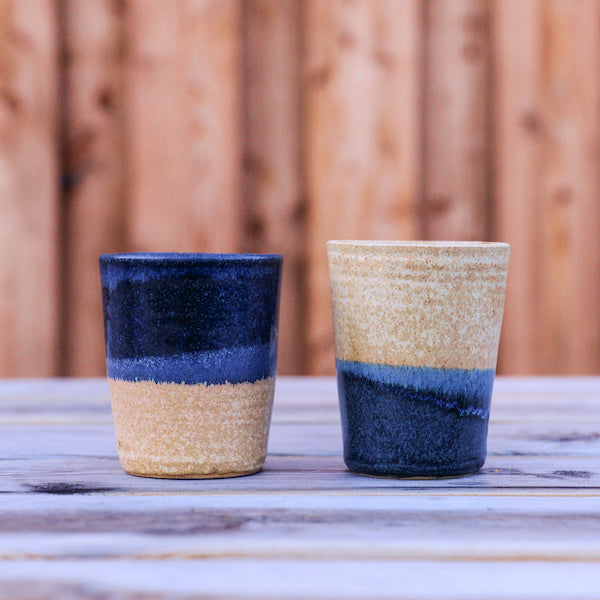 Two ceramic flat white tumblers on a wooden table