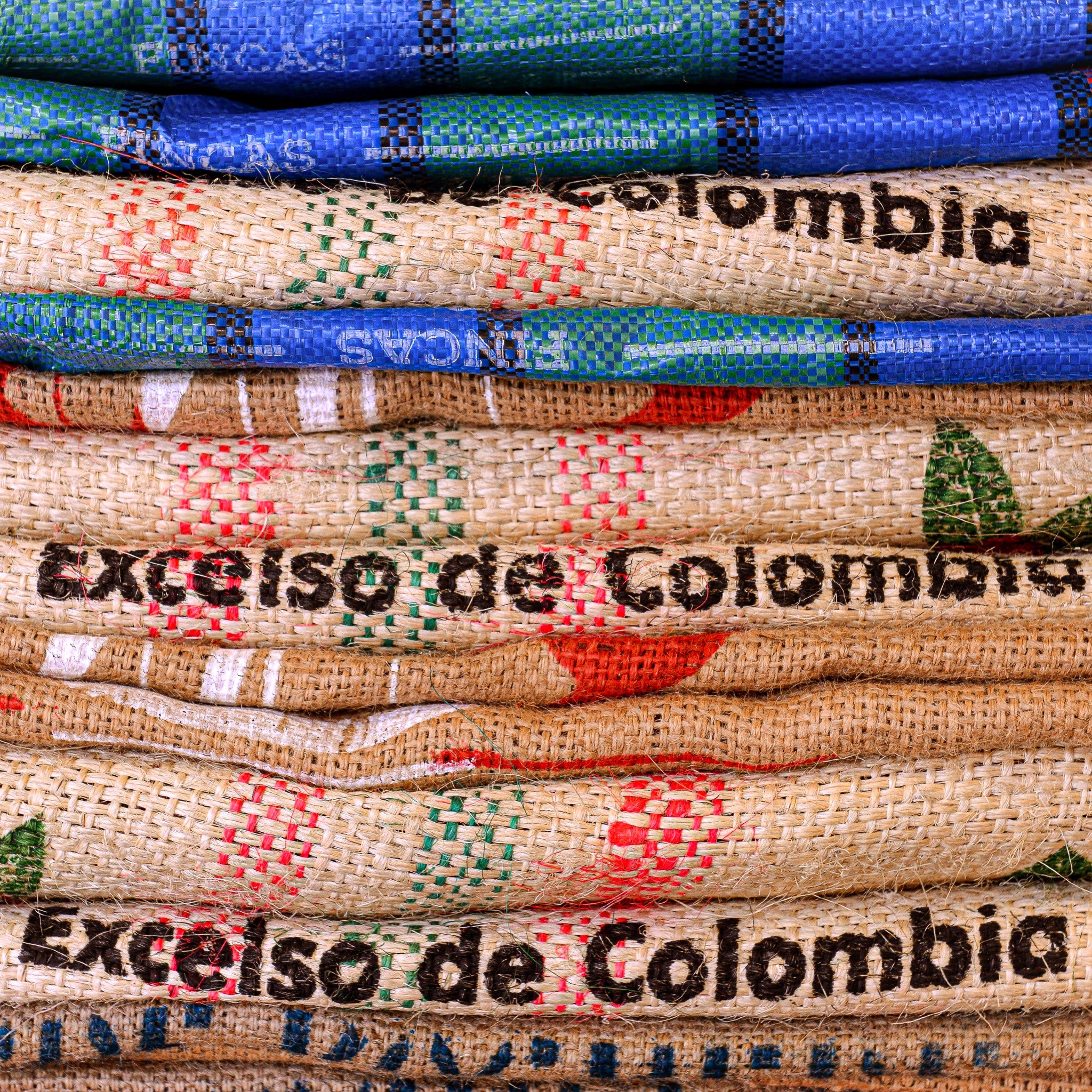 Close up of a pile of folded green coffee sacks from various countries in various colours