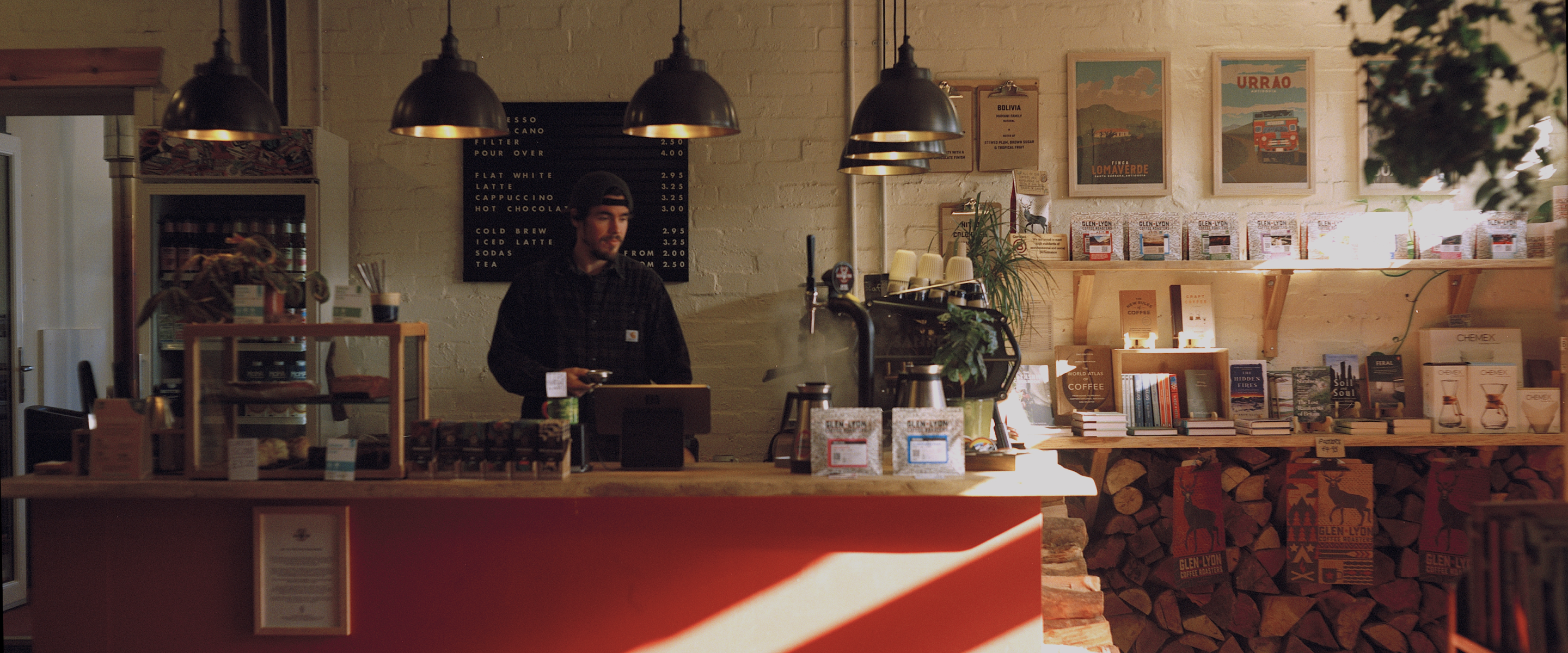 A wide interior shot of Glen Lyon Coffee Roasters' roastery cafe with a barista standing behind the bar
                                        