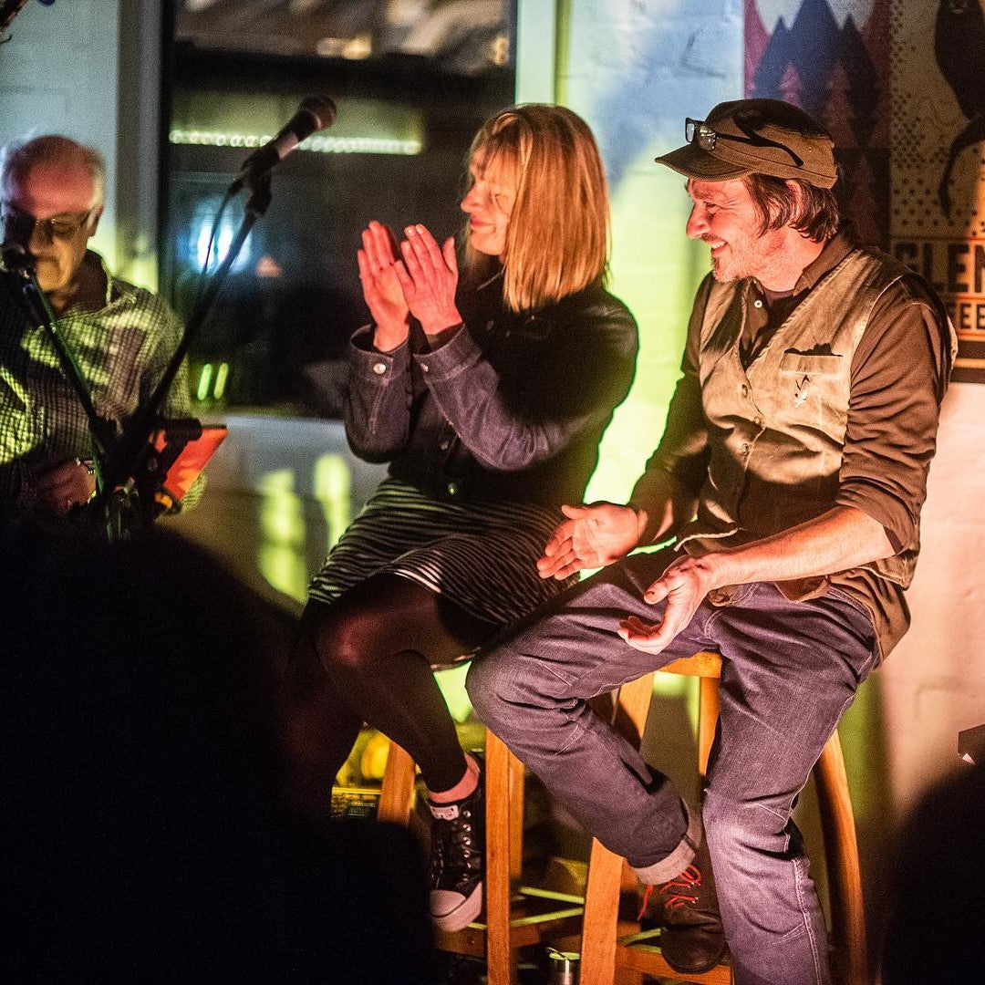 Two people on stools applauding inside the Glen Lyon Coffee roastery cafe during a Live At The Roastery gig