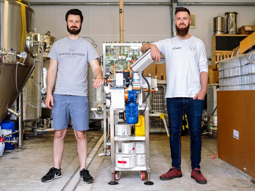 Jack and Conall of Wasted Degrees brewing pose in front of their industrial brewing and canning equipment.