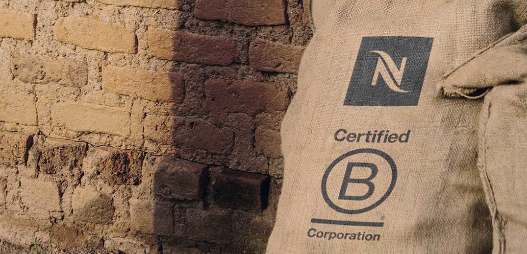 A bag of green coffee sporting the logos of Nespresso and B Corp against a brick background