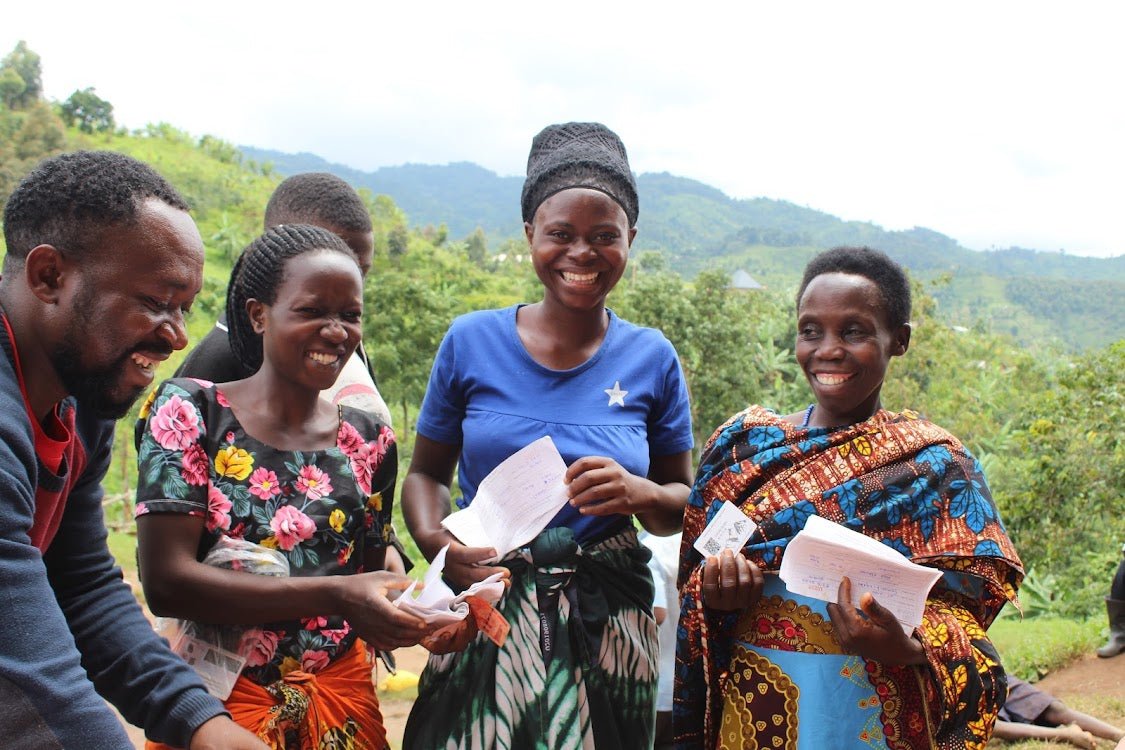A happy group of Ugandans stand near a tranquil coffee farm and share notes.