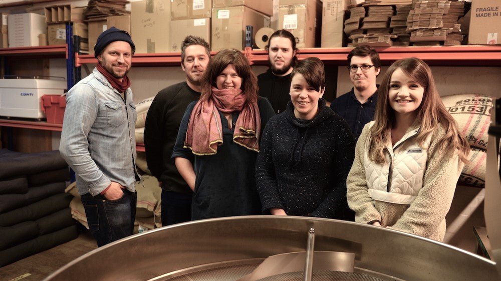 Glen Lyon Coffee team pose in the roastery with the roaster cooling tray in the foreground