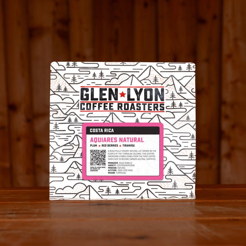 A 250g bag of Aquiares Natural from Glen Lyon Coffee Roasters coffee sits on a wooden table with a slatted wood background.