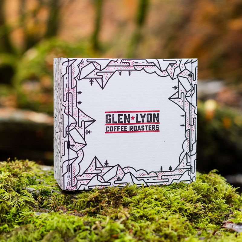 The side of the same box with the Glen Lyon Coffee Roasters logo and black mountain and tree designs sits on a bed of moss.