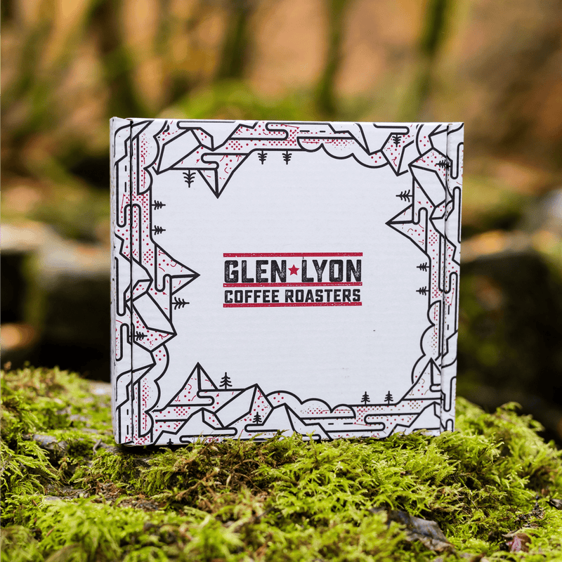 A white and black box with the Glen Lyon Coffee Roasters logo and black mountain and tree designs sits on a bed of moss.