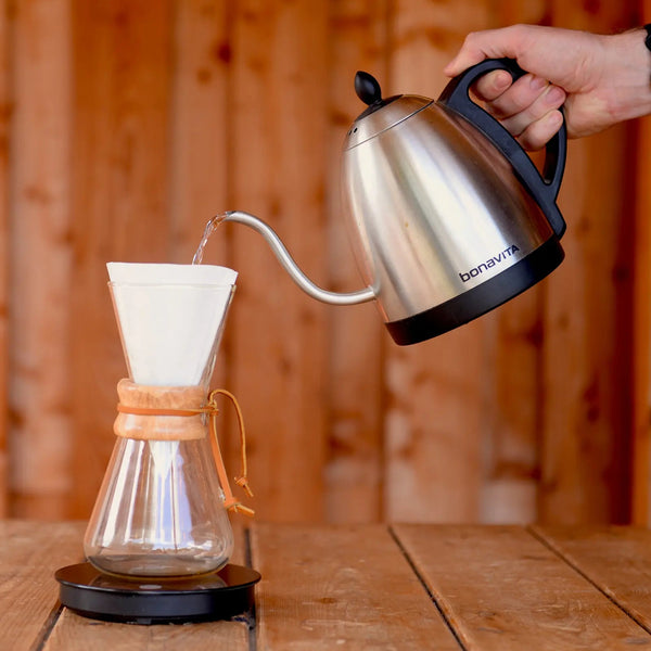 Hand pouring boiled water from a goose neck kettle into a Chemex sitting atop a scale.