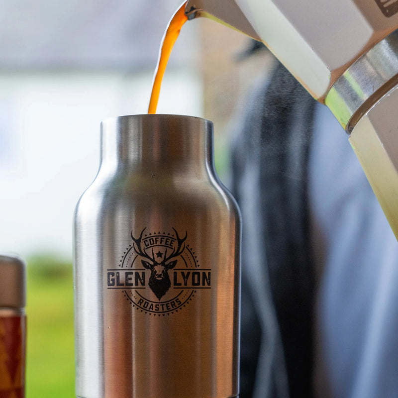 A person pouring coffee from a stainless steel moka pot straight into an insulated flask with laser engraved Glen Lyon logo.