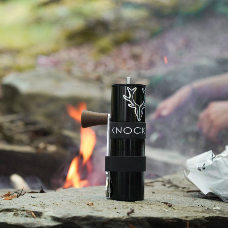 A campfire smokes in the background and an Aerspeed grinder with added sticker sits on a rock awaiting use.