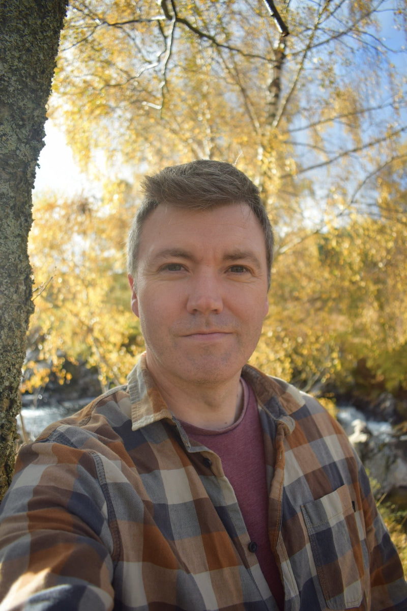 Anthony McCluskey, a man with short brown hair and round face, stands amongst the yellowing autumn trees in Glen Lyon.