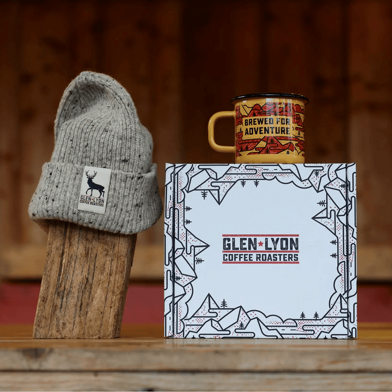 A speckled grey Scottish wool hat with Glen Lyon Coffee logo and an orange and red enameled camp mug sit atop a branded box.