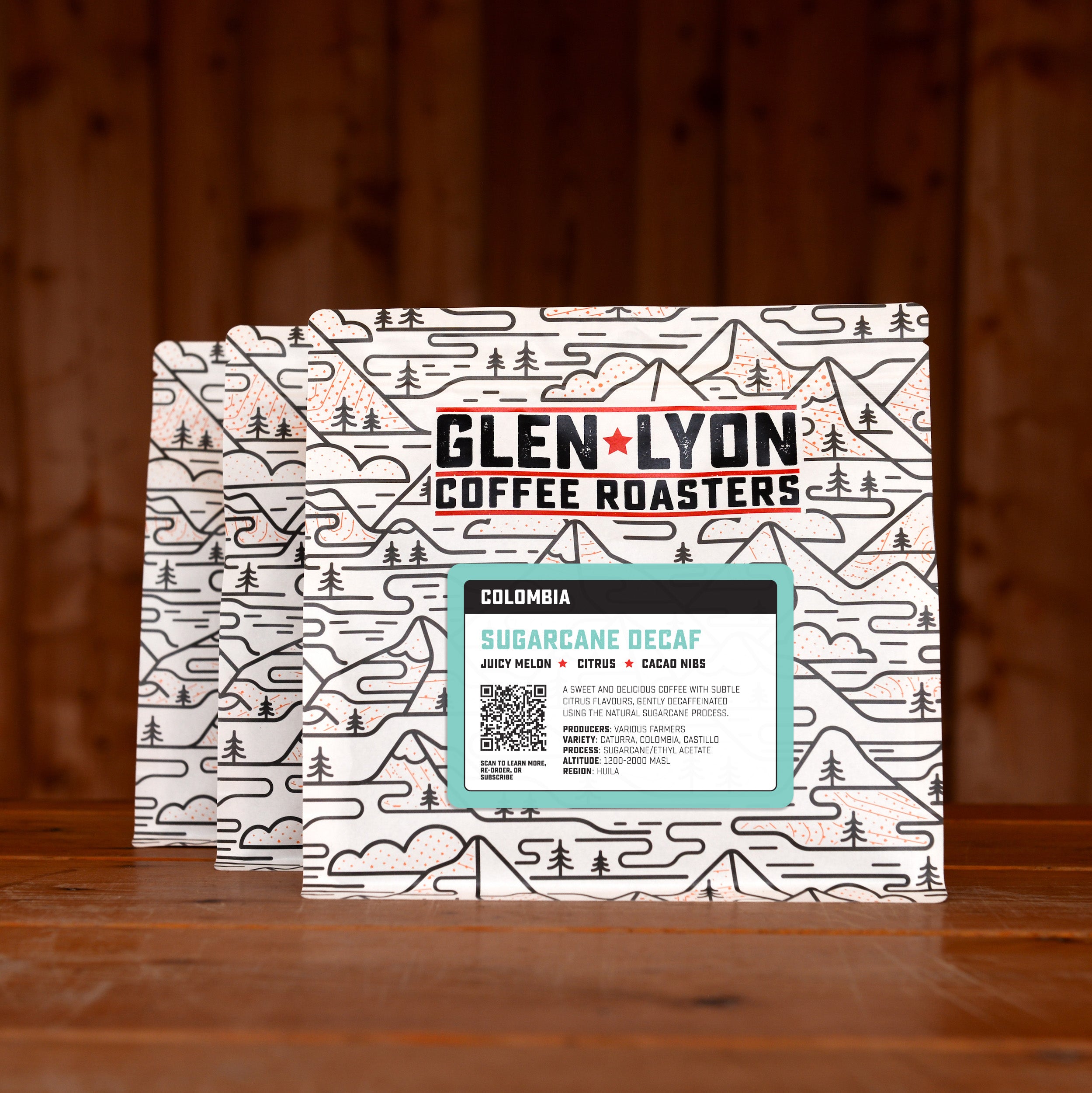 3 bags of Decaf subscription labelled speciality coffee from Glen Lyon Coffee Roasters against a warm wood-tinged background