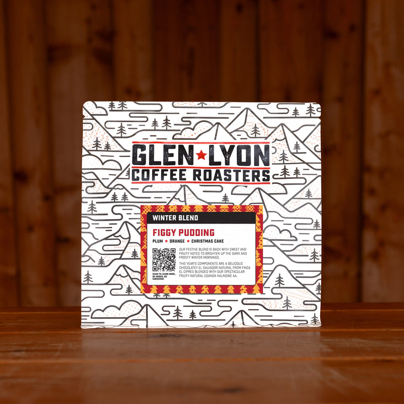 A 250g bag of Figgy Pudding from Glen Lyon Coffee Roasters coffee sits on a wooden table with a slatted wood background.