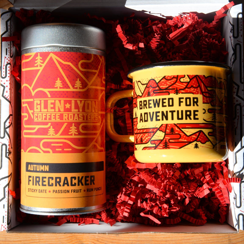 A metal 220g tin of Figgy Pudding and an orange and red enameled camp mug with black mountain design inside a gift box.