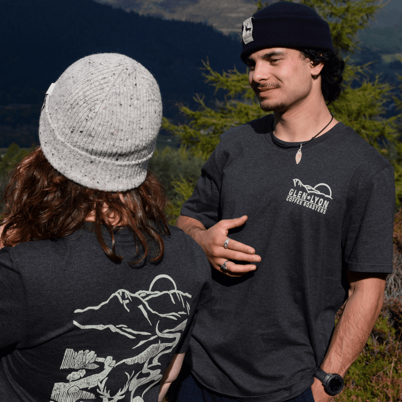 Pretam shows off the front of the shirt which features a Glen Lyon Coffee Roasters logo with a mountain and sun design.
