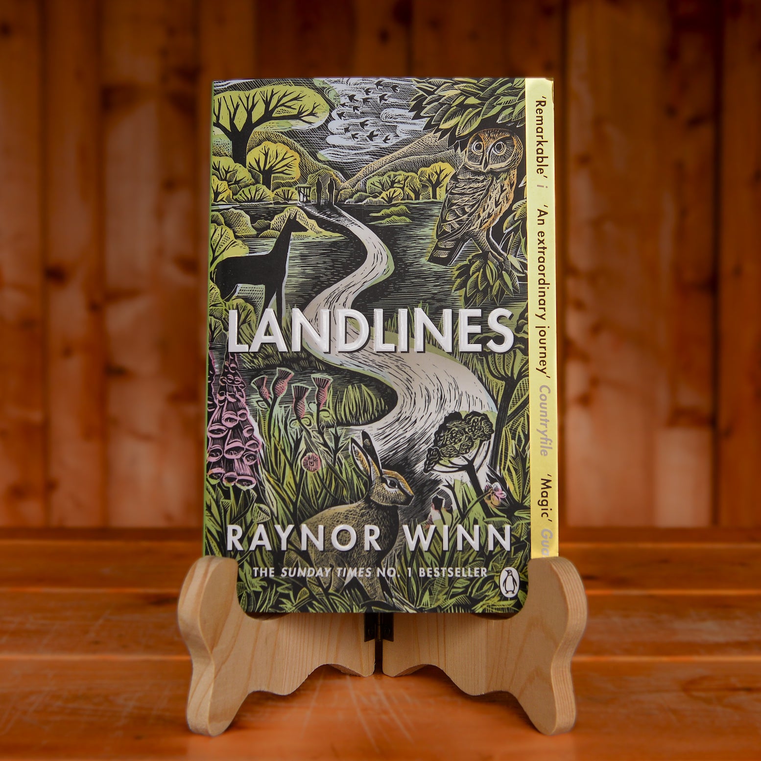 The book Landlines by Raynor Winn displayed on a book stand on a wooden table