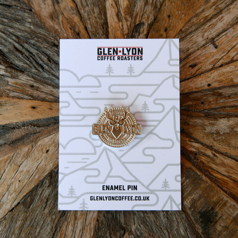 A silver Glen Lyon stag logo pin sits on a card on a wood table.