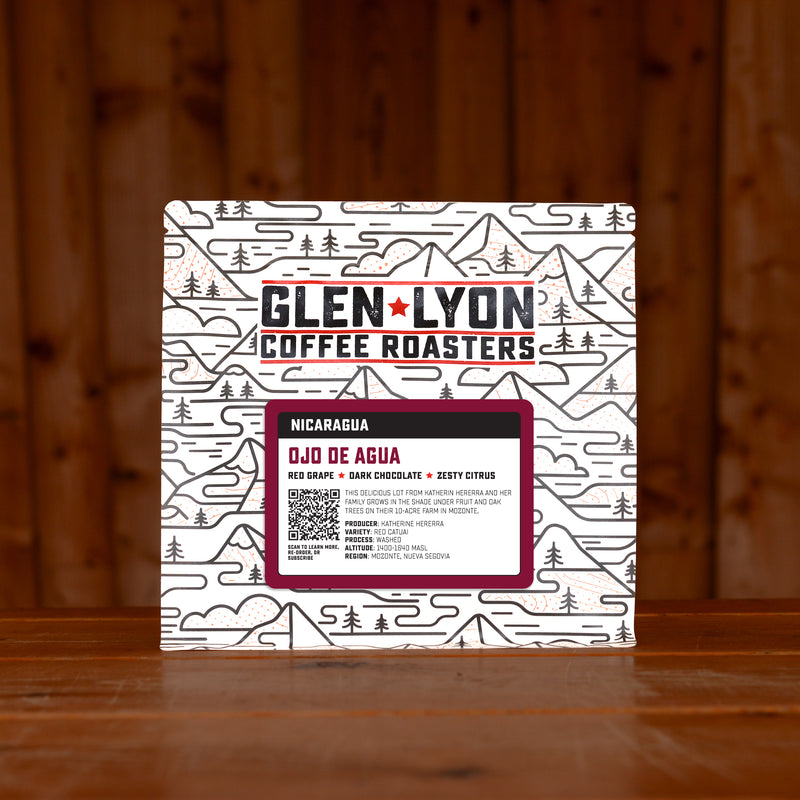 A 250g bag of Ojo de Agua from Glen Lyon Coffee Roasters coffee sits on a wooden table with a slatted wood background.