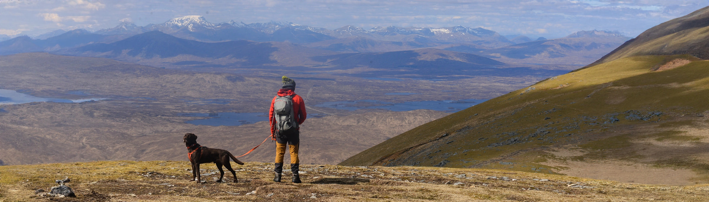 Man wearing backpack looking out over hills with black dog.