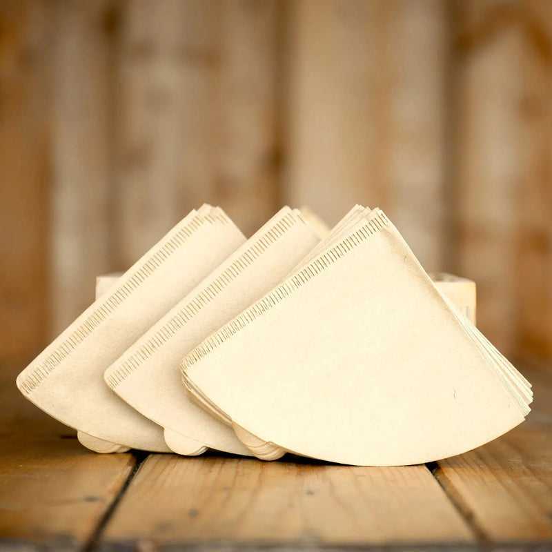 A pack of unbleached, brown conical V60 filters sit on a wooden table with wood background.