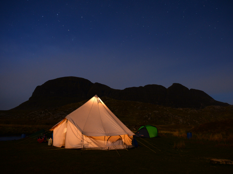 Mobile version of a lit-up tent at night under the stars with a hill behind