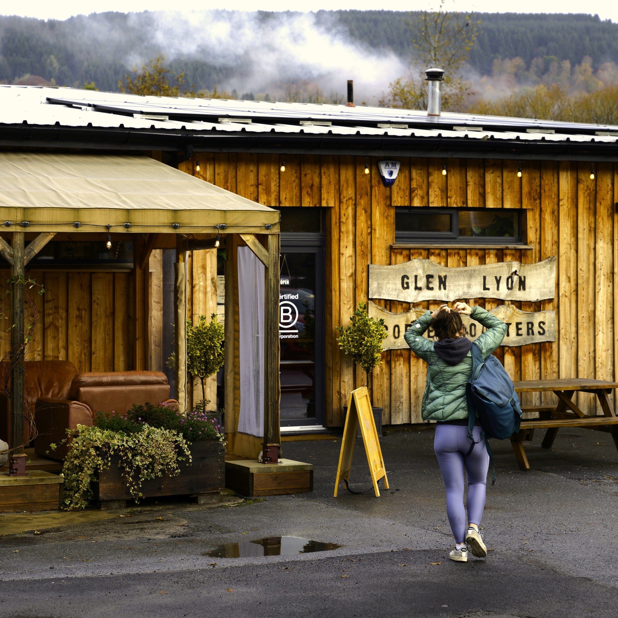 A square exterior shot of a customer carrying a bag walking towards the Glen Lyon Coffee roastery cafe on a rainy day