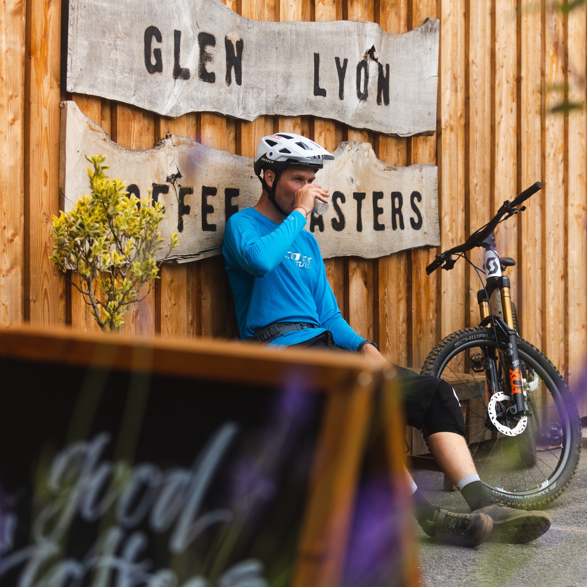 A mountain biker sits on a bench outside the Glen Lyon Coffee roastery cafe enjoying a delicious speciality coffee