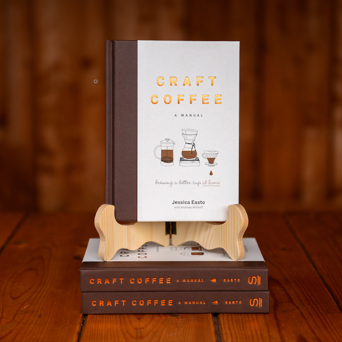 The book Craft Coffee: A Manual by Jessica Easto displayed on a book stand on a wooden table