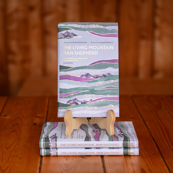 The book The Living Mountain by Nan Shepherd displayed on a book stand on a wooden table