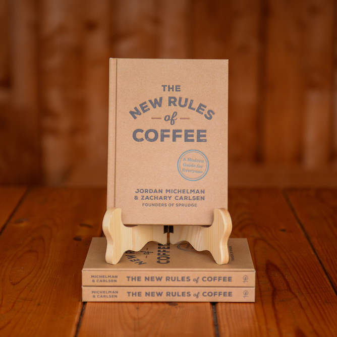The book The New Rules of Coffee by Jordan Michelman and Zachary Carlsen displayed on a book stand on a wooden table