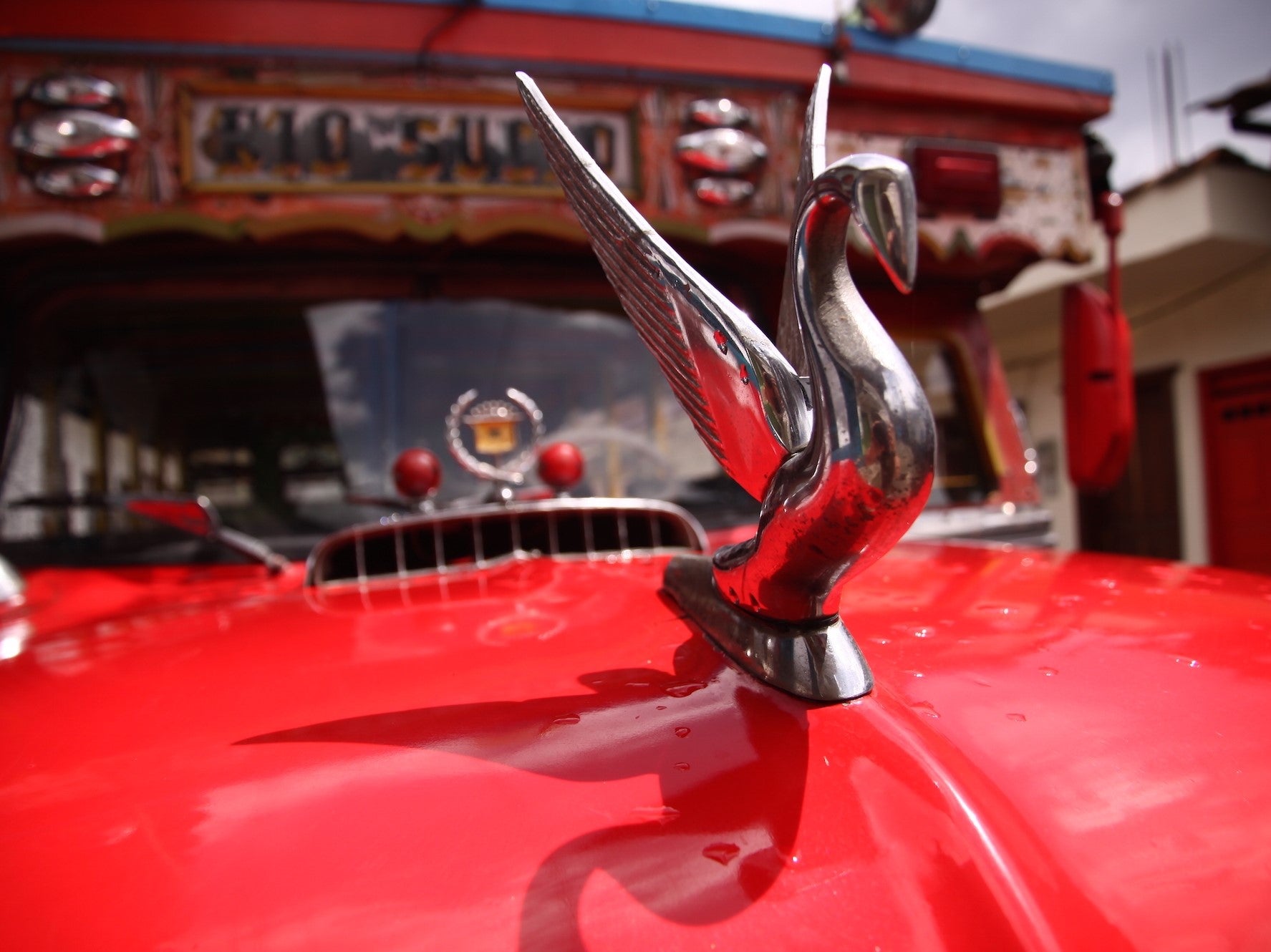 Mobile version of: Close up of a red vintage car's hood ornament in Colombia