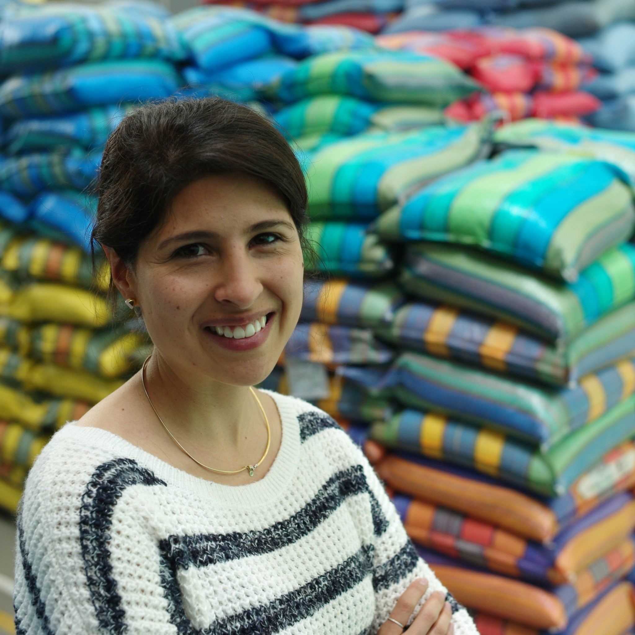 A smiling person in a warehouse with arms folded looks towards the camera with sacks of speciality coffee piled behind