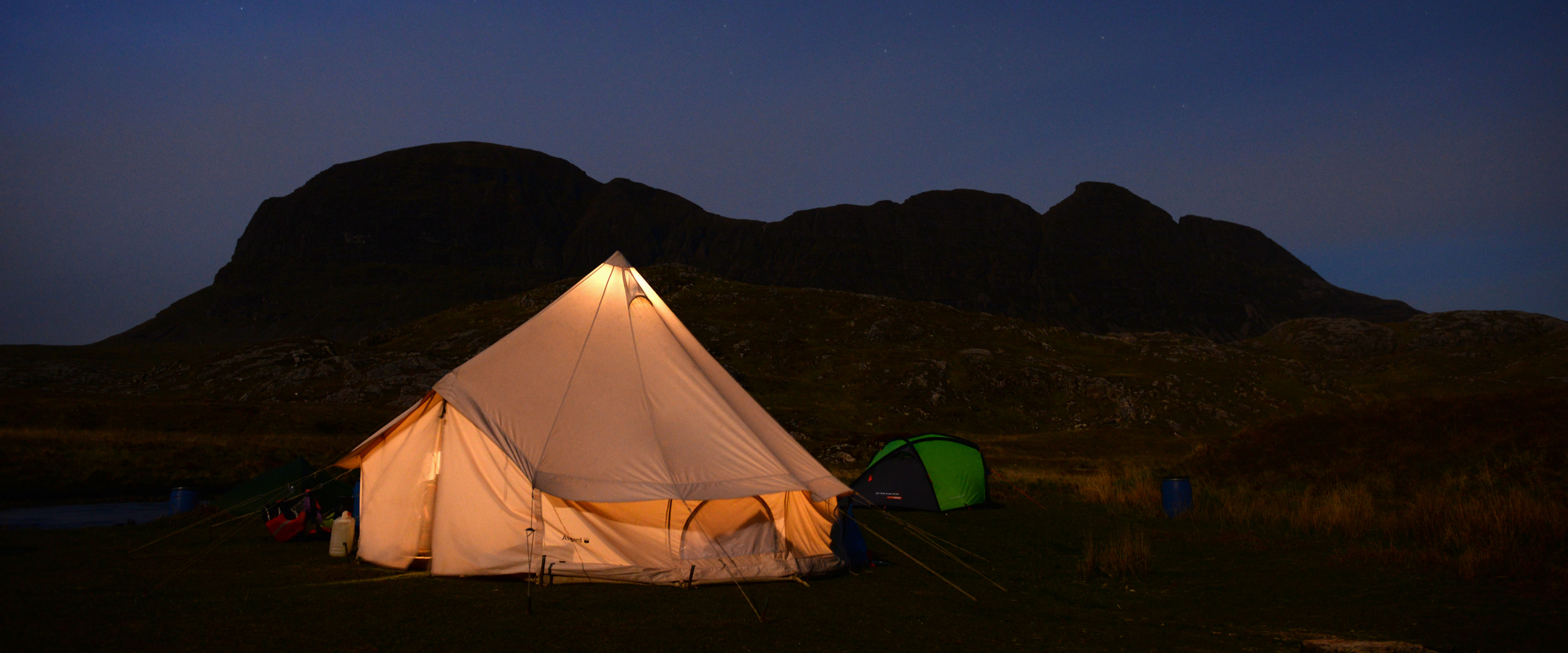 A lit-up tent at night under the stars with a hill behind