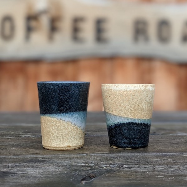 Two ceramic flat white tumblers on a wooden table with the Glen Lyon Coffee sign in the background