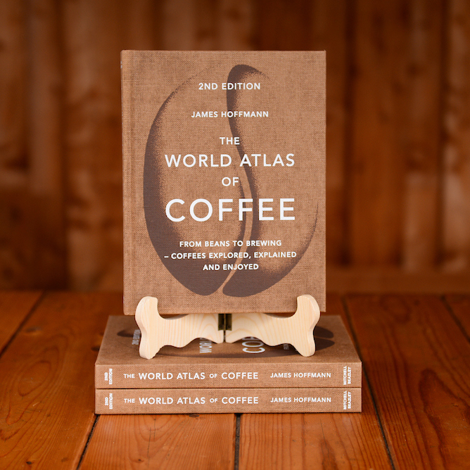 The book The World Atlas of Coffee by James Hoffmann displayed on a book stand on a wooden table